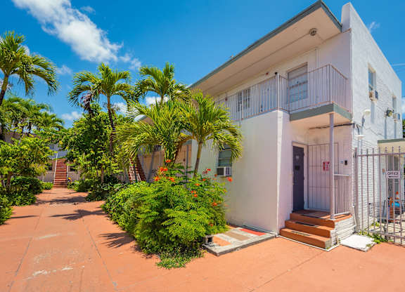 A white two-story house with a balcony and a gate.
