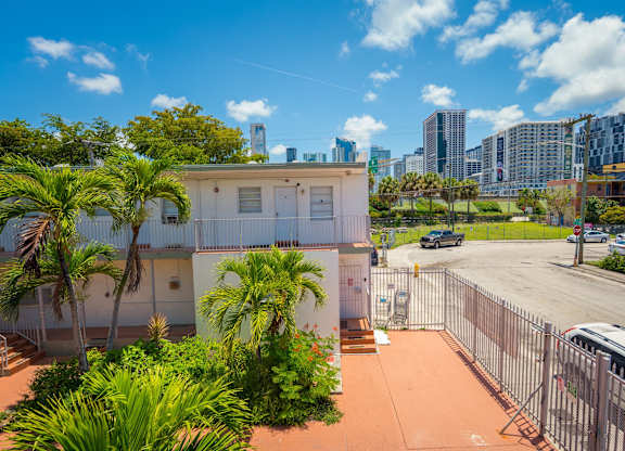 A white building with a fence and palm trees in front of a city skyline.