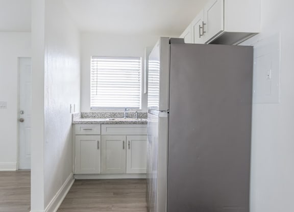 A kitchen with a refrigerator, cabinets, and a window with blinds.