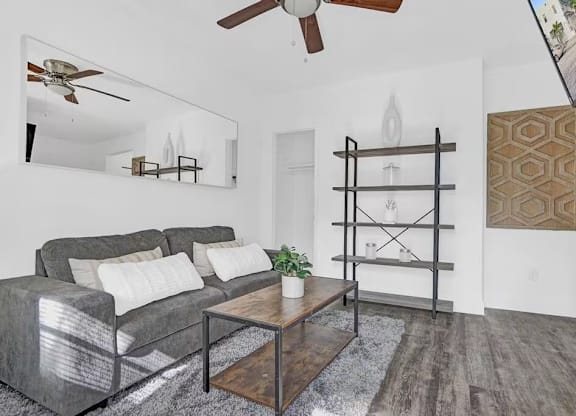 A modern living room with a grey couch, a wooden coffee table, and a mirror on the wall.