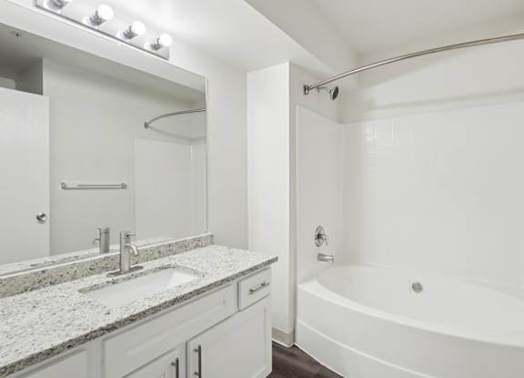 A white bathroom with a sink, mirror, and bathtub.