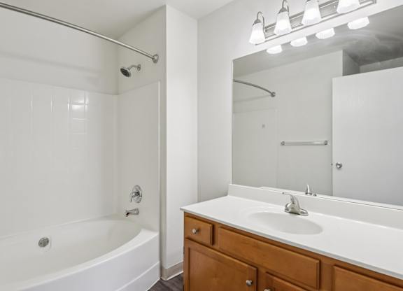 A white bathroom with a tub, sink, and mirror.