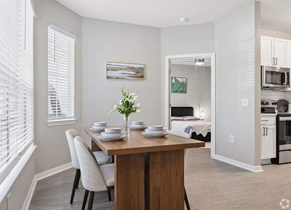 A dining room with a table set for two and a view of the kitchen in the background.