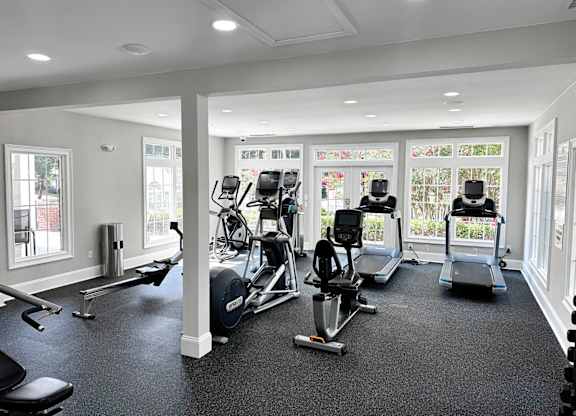 A spacious gym with a variety of cardio equipment and a view of the outdoors through the windows.