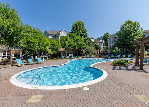 A swimming pool surrounded by trees and lounge chairs.