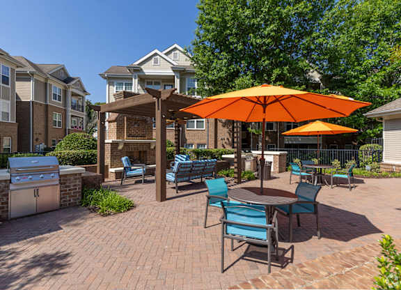 A patio with a table and chairs and an orange umbrella.