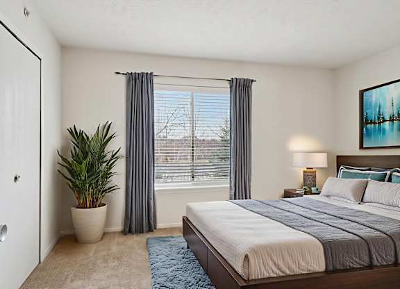 A bedroom with a large bed, a potted plant, and a painting on the wall.
