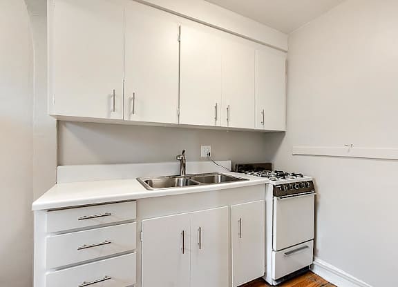 A white kitchen with a sink, stove, and cabinets.