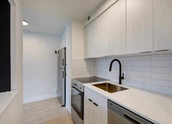 A kitchen with white cabinets and a black faucet.