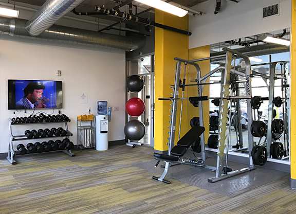 A gym with a variety of equipment including a weight bench, a rowing machine, and a television.
