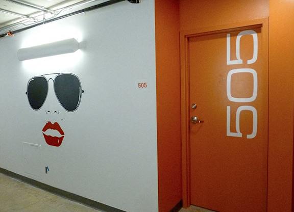 A white wall with a drawing of a woman's face and a door with the number 505 on it.