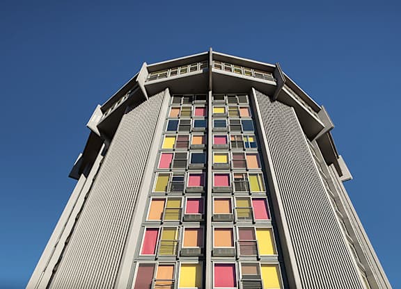 A tall building with a row of windows in red, yellow, orange, and pink.