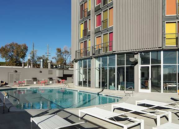 A swimming pool is surrounded by sun loungers in front of a modern building.
