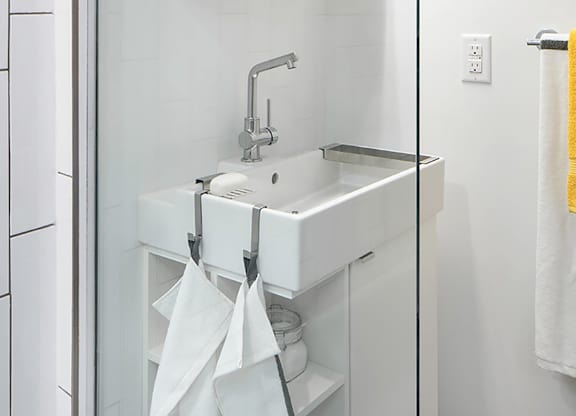 A white sink with a silver faucet and a white cabinet with a glass door.