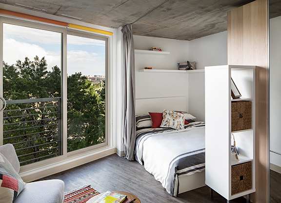 A bedroom with a bed, a chair, and a window with a view of trees.