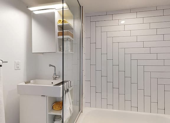 A white sink with a white cabinet and a white bathtub in a bathroom.