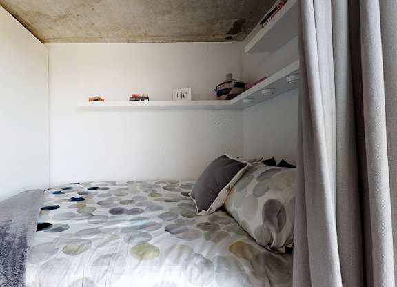 A bed with a grey and white patterned comforter and a grey pillow is in the foreground of the image.