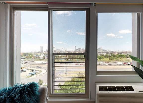 A view of a cityscape through a window with a blue cushion on the left and a plant on the right.