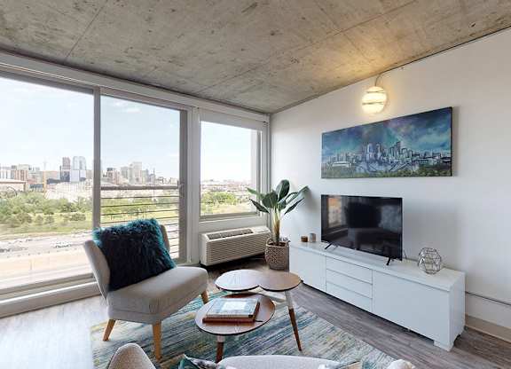 A living room with a chair, a table, a potted plant, and a painting on the wall.
