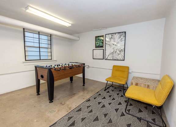A room with a foosball table, two chairs, and a bench.