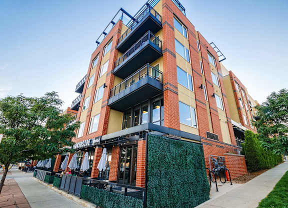 A multi-story building with balconies and a green fence in front.