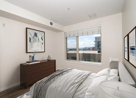 A bedroom with a bed, nightstand, and a window overlooking a cityscape.