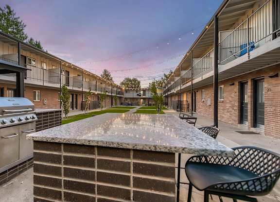 A patio with a grill and chairs is surrounded by apartment buildings.