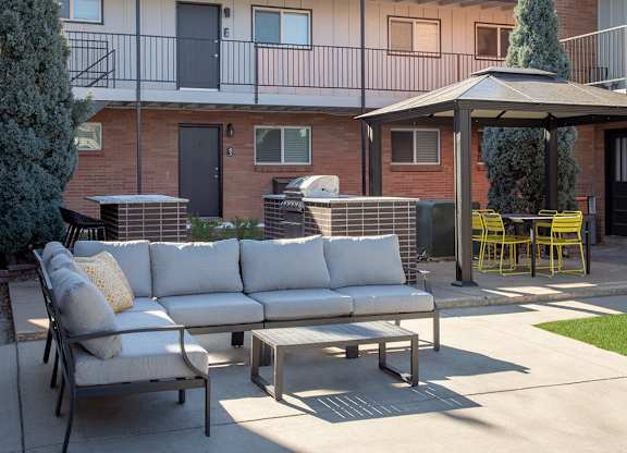 A patio with a white couch, yellow chairs, and a table with a tree in a pot.