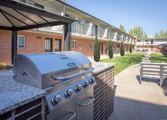 A silver grill is on a patio with a building in the background.