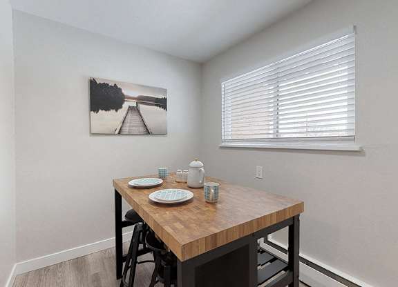 A dining table with four chairs and a painting on the wall.