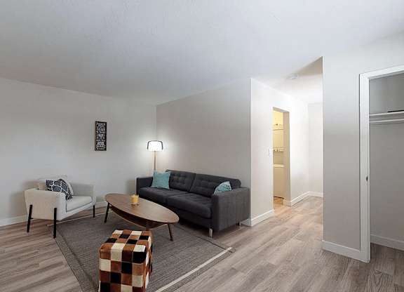 A living room with a black couch, a white chair, a coffee table, and a potted plant.