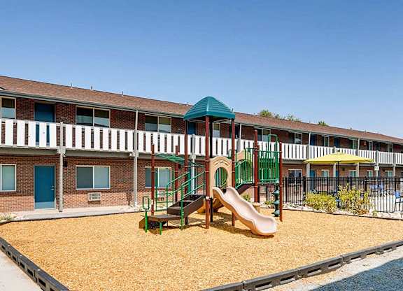 A playground with a slide and sandbox in front of a building.