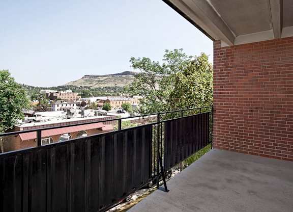 A balcony with a black railing overlooks a town with a mountain in the distance.
