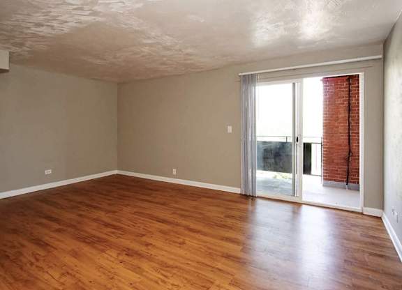 A room with wooden floors and a sliding glass door leading to a balcony.
