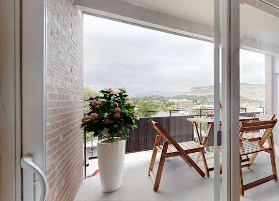 A white vase with pink flowers sits on a patio next to two wooden chairs.