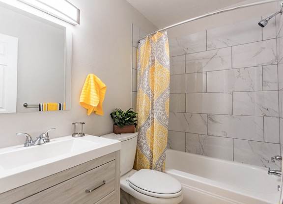 A bathroom with a white toilet, sink, and a yellow shower curtain.