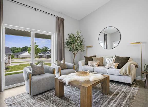 A living room with a grey couch, a coffee table, and a round mirror on the wall.
