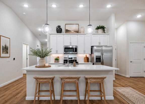 A kitchen with white cabinets and a white island with three bar stools.
