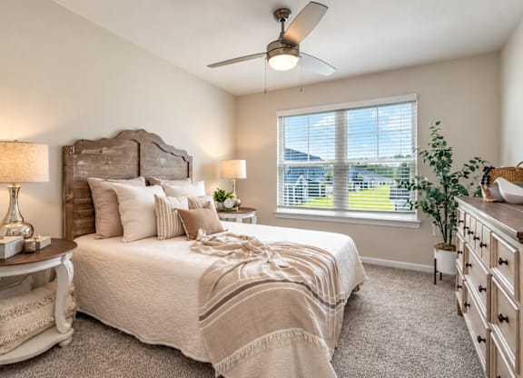 A bedroom with a large bed, a ceiling fan, and a window with blinds.