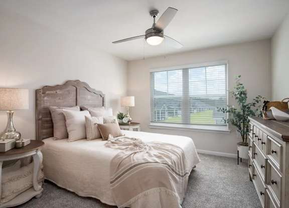 A bedroom with a large bed, a ceiling fan, and a window with blinds.