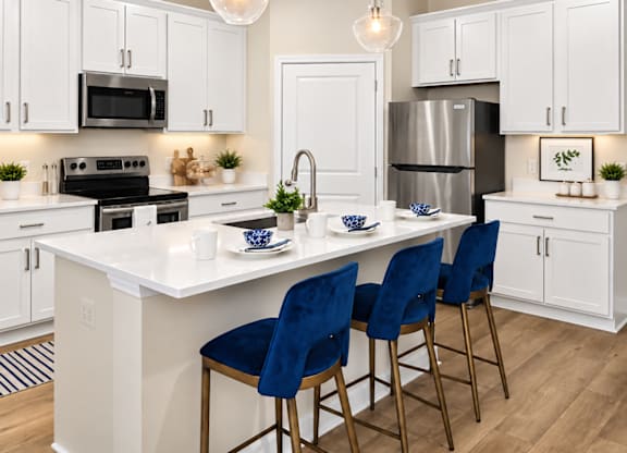 A kitchen with white cabinets and a white island with blue chairs.