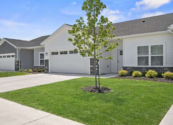 A tree stands in a grassy area in front of a house.