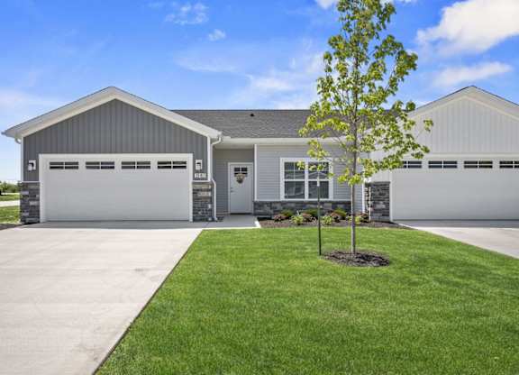 A house with a grey garage door and a tree in front.