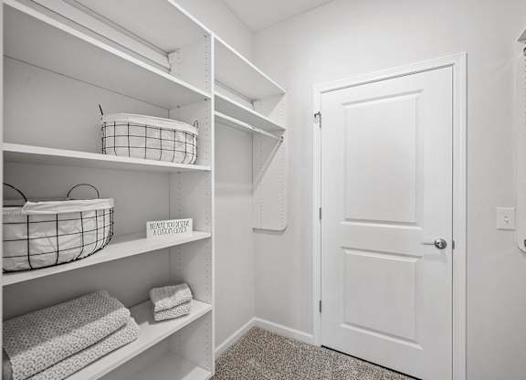 A white closet with a basket on the shelf and towels on the shelf.