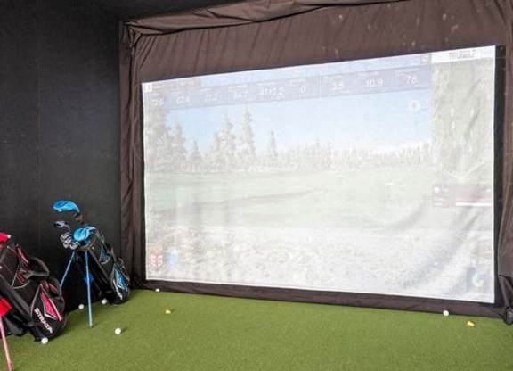 A golf simulator room with a screen showing a golf course.