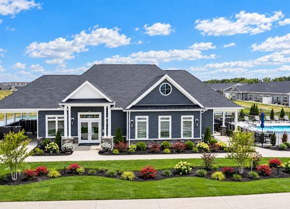A house with a grey roof and white trim is surrounded by a well-manicured lawn and a variety of plants.