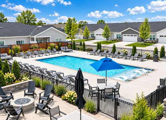 A pool surrounded by chairs and umbrellas with houses in the background.