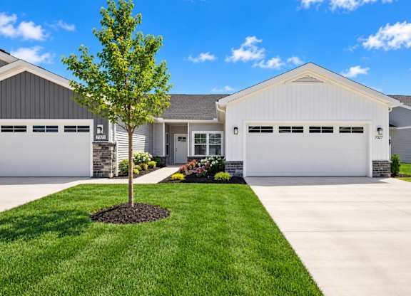 A two-story house with a garage and a tree in front.