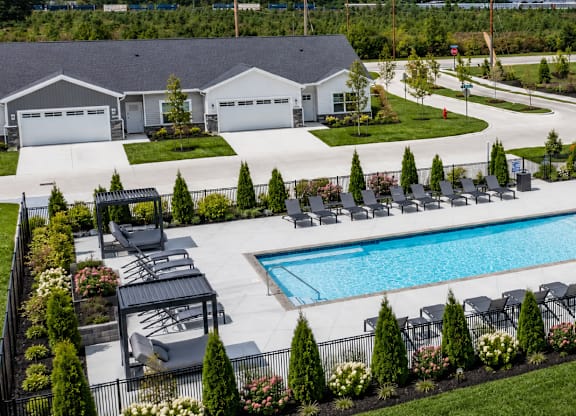 A large outdoor swimming pool surrounded by a patio area with chairs and a small building.