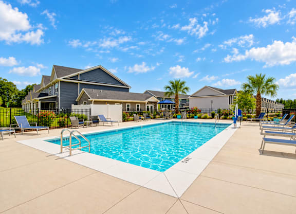 A swimming pool surrounded by lounge chairs and palm trees.